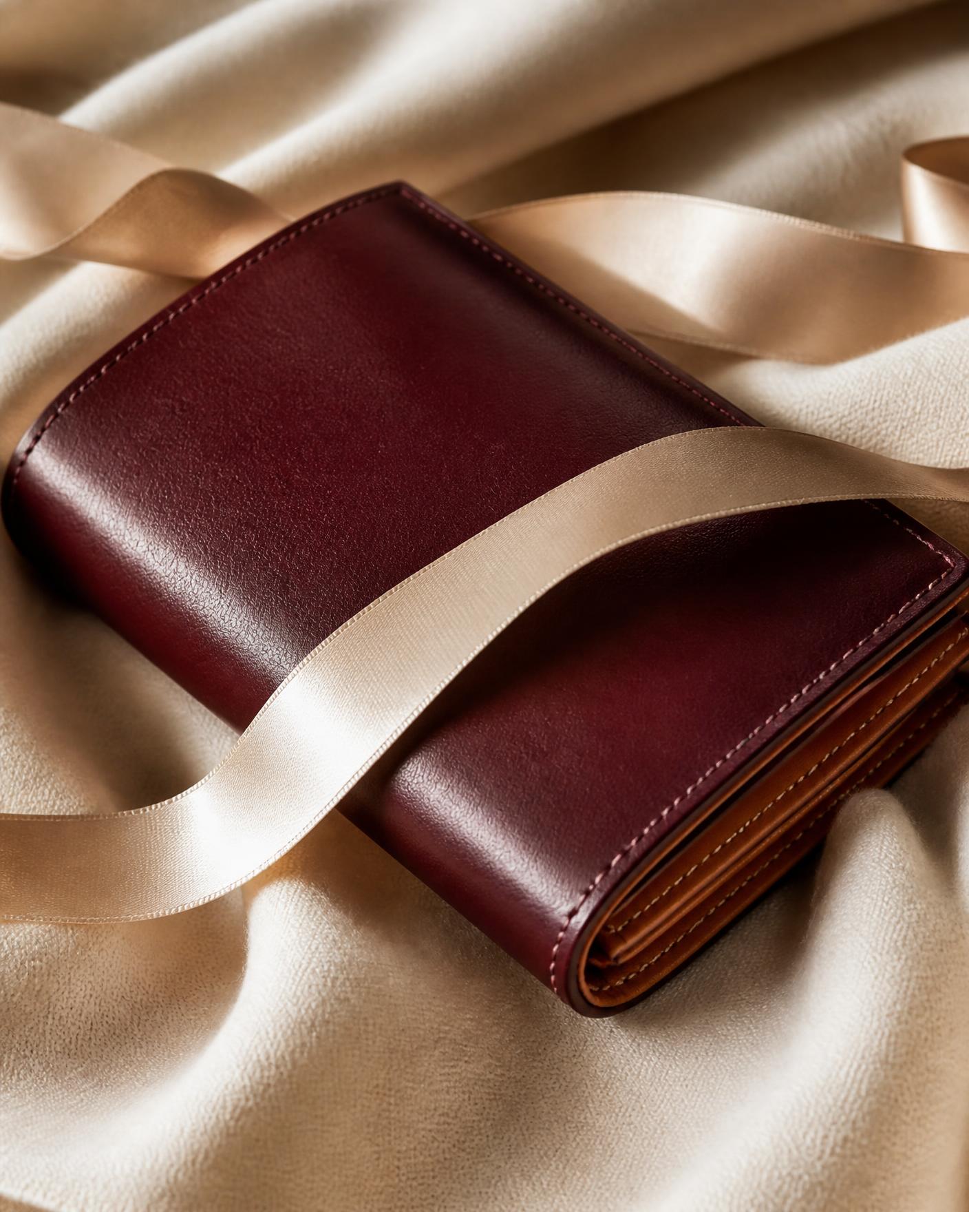Oxblood leather wallet with tan interior wrapped in a cream ribbon